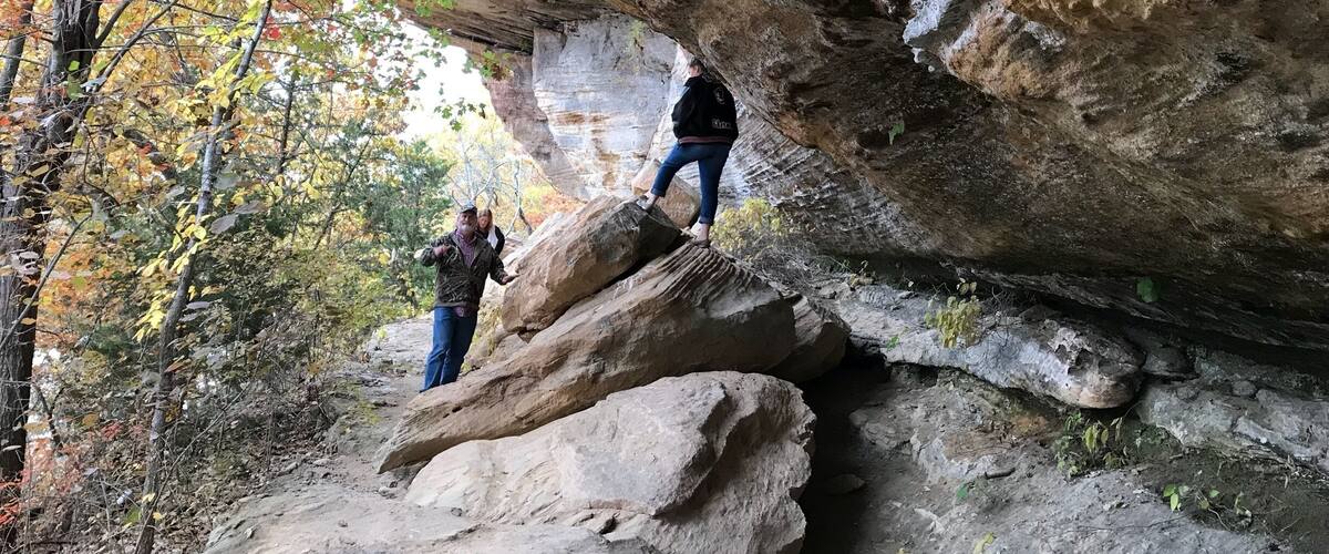 A person climbing a large rock formation surrounded by autumn foliage.
