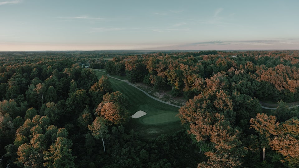 A golf course surrounded by dense forest with autumn foliage.