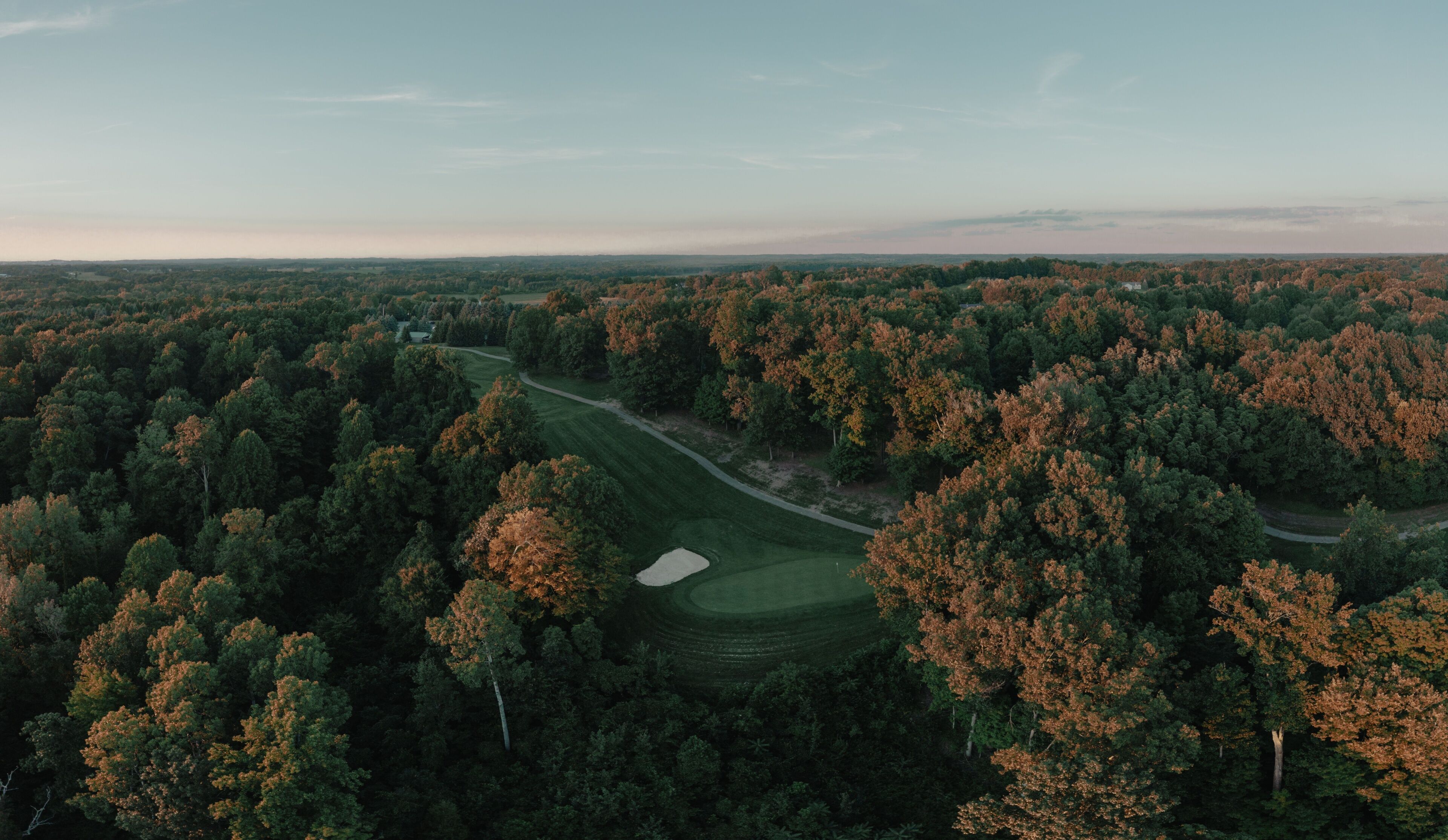 A golf course surrounded by dense forest with autumn foliage.