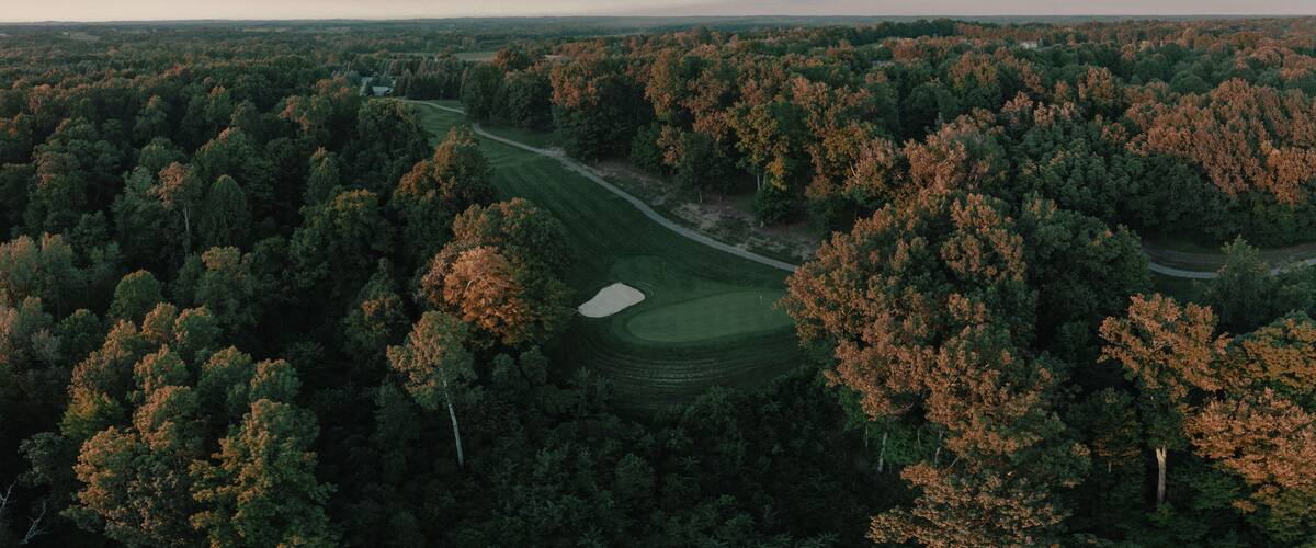 A golf course surrounded by dense forest with autumn foliage.