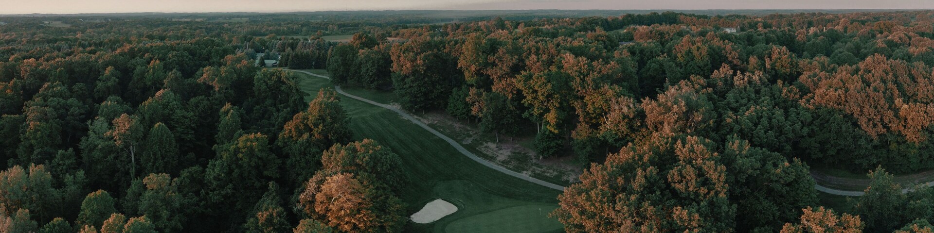 A golf course surrounded by dense forest with autumn foliage.
