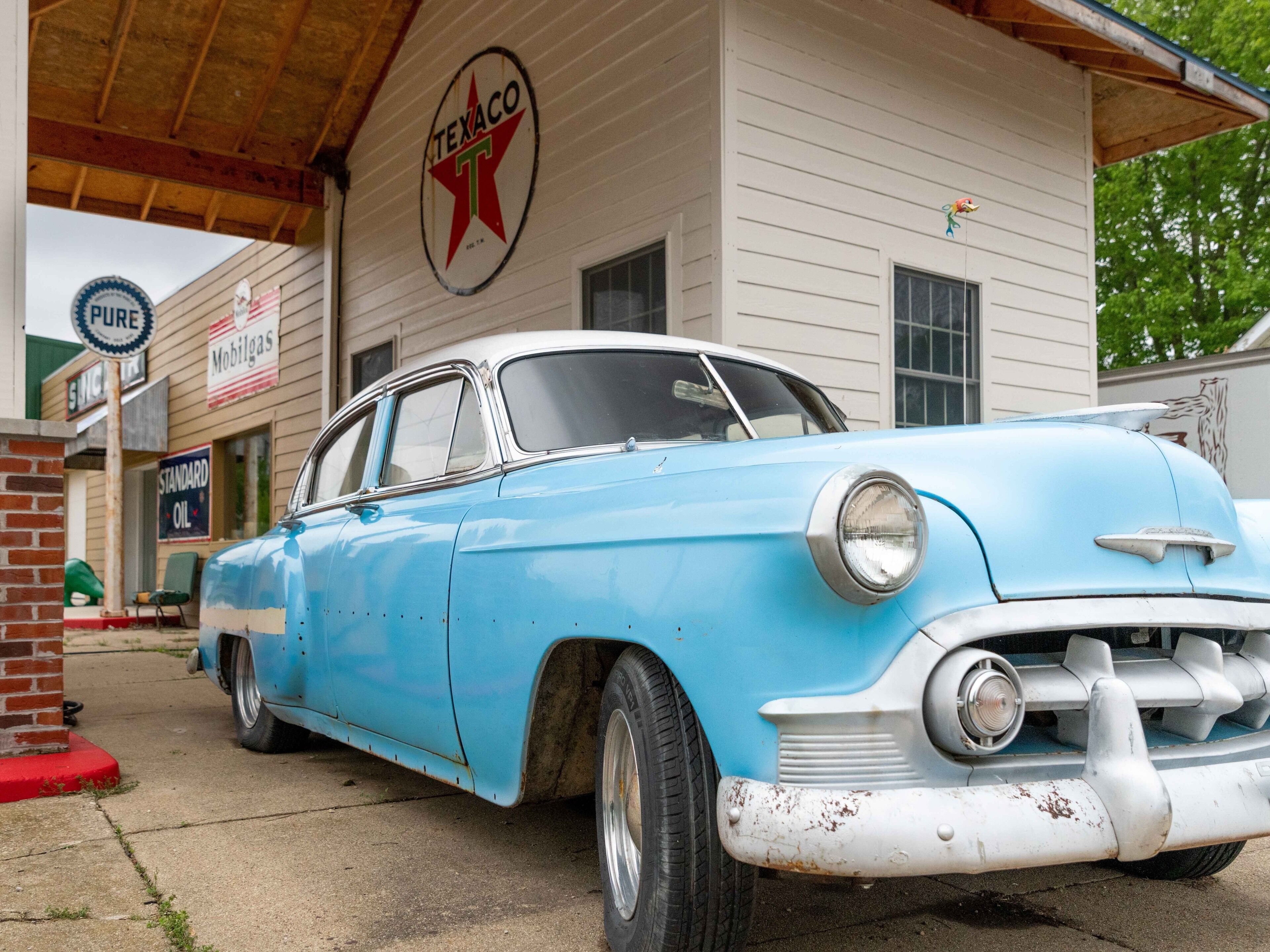 A vintage blue car parked in front of a Texaco gas station.