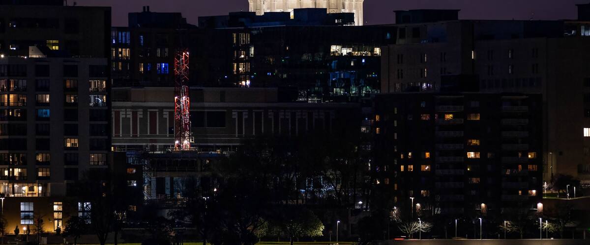 A cityscape at dusk with a prominent illuminated dome structure in the background, reflecting on the water in the foreground.