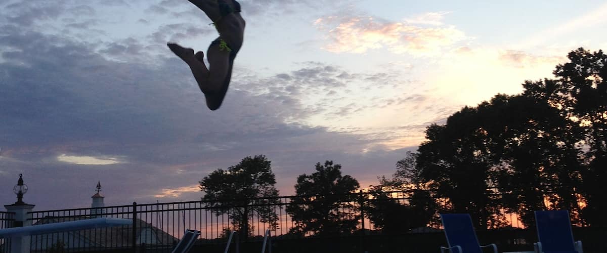 A person jumping into a swimming pool at sunset with a cloudy sky in the background.