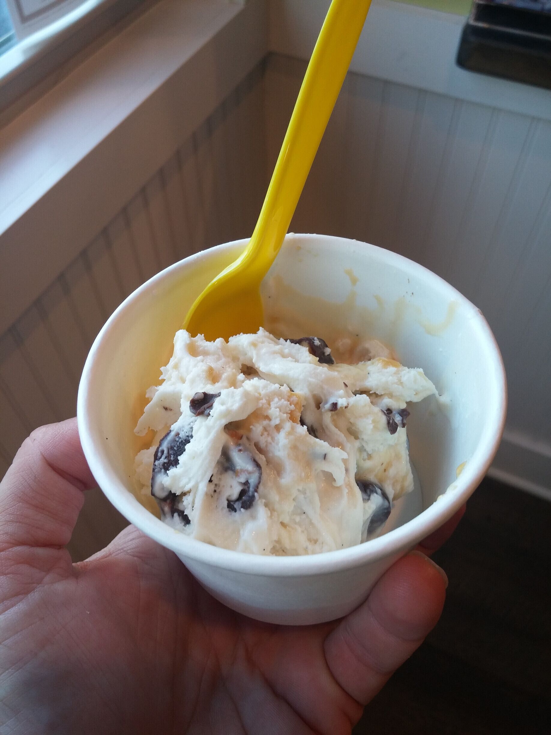 A hand holding a bowl of ice cream with a yellow spoon.