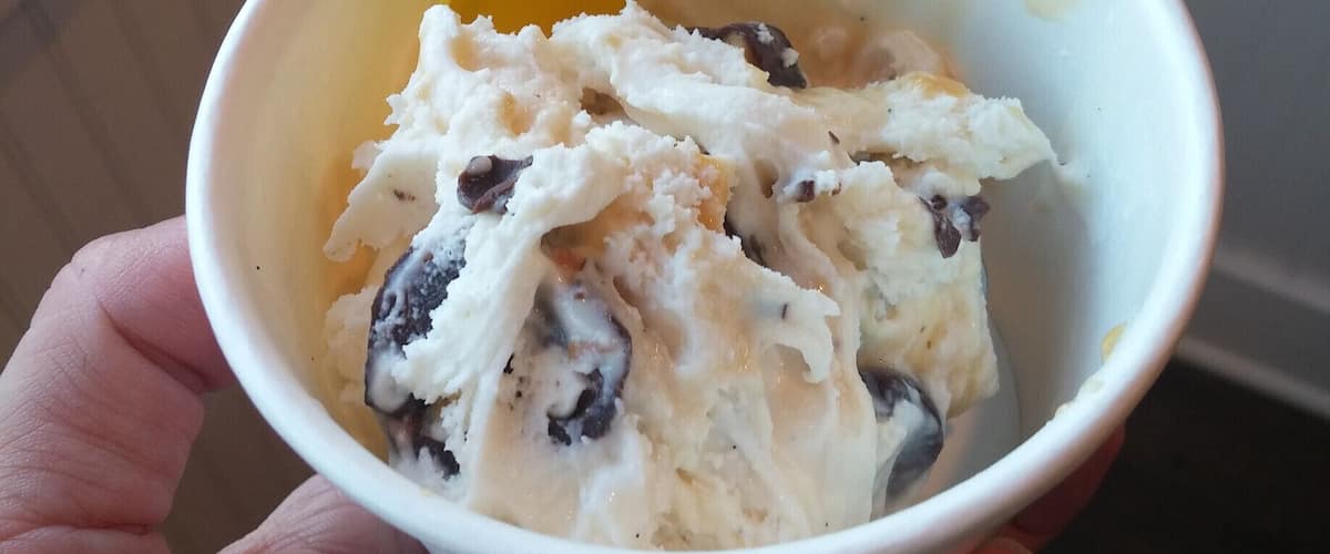 A hand holding a bowl of ice cream with a yellow spoon.