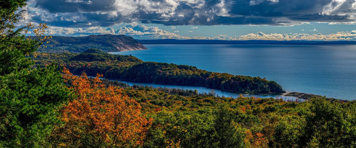 A coastal landscape with a large body of water, dense forest, and prominent cloud formations.