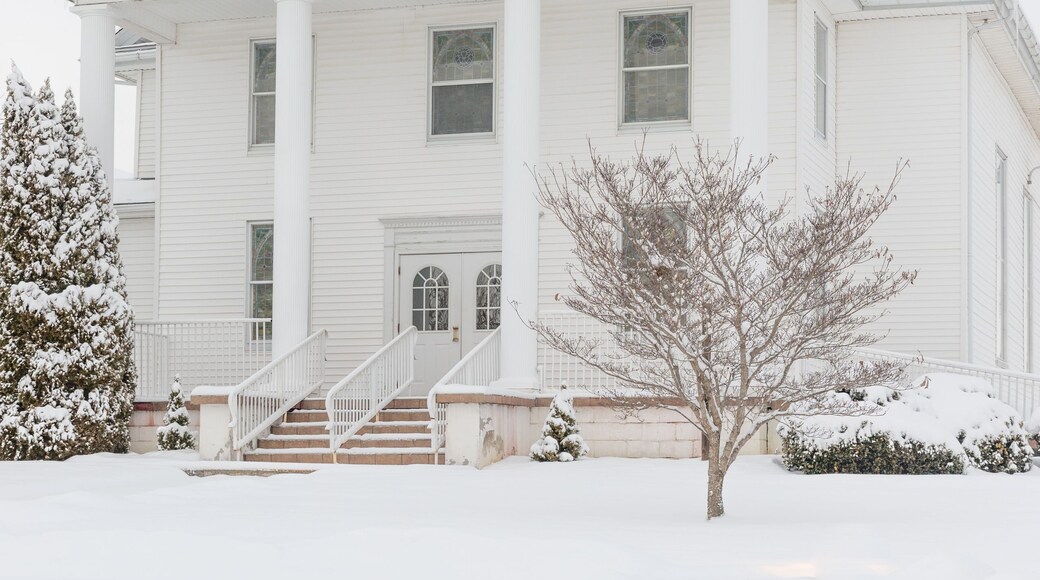 A white church with a steeple and a cross on top, surrounded by snow-covered trees.