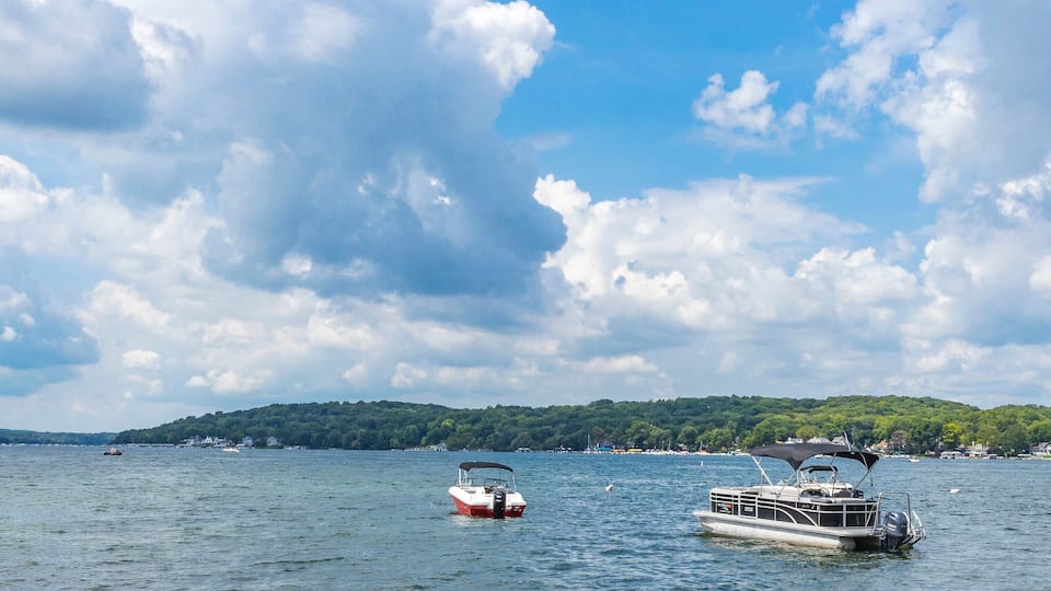 A pontoon boat and pleasure boat anchored in a large lake with white cumulus clouds and a blue sky.