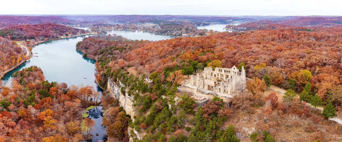 A river winding through a forested valley with a historic castle on a cliff.