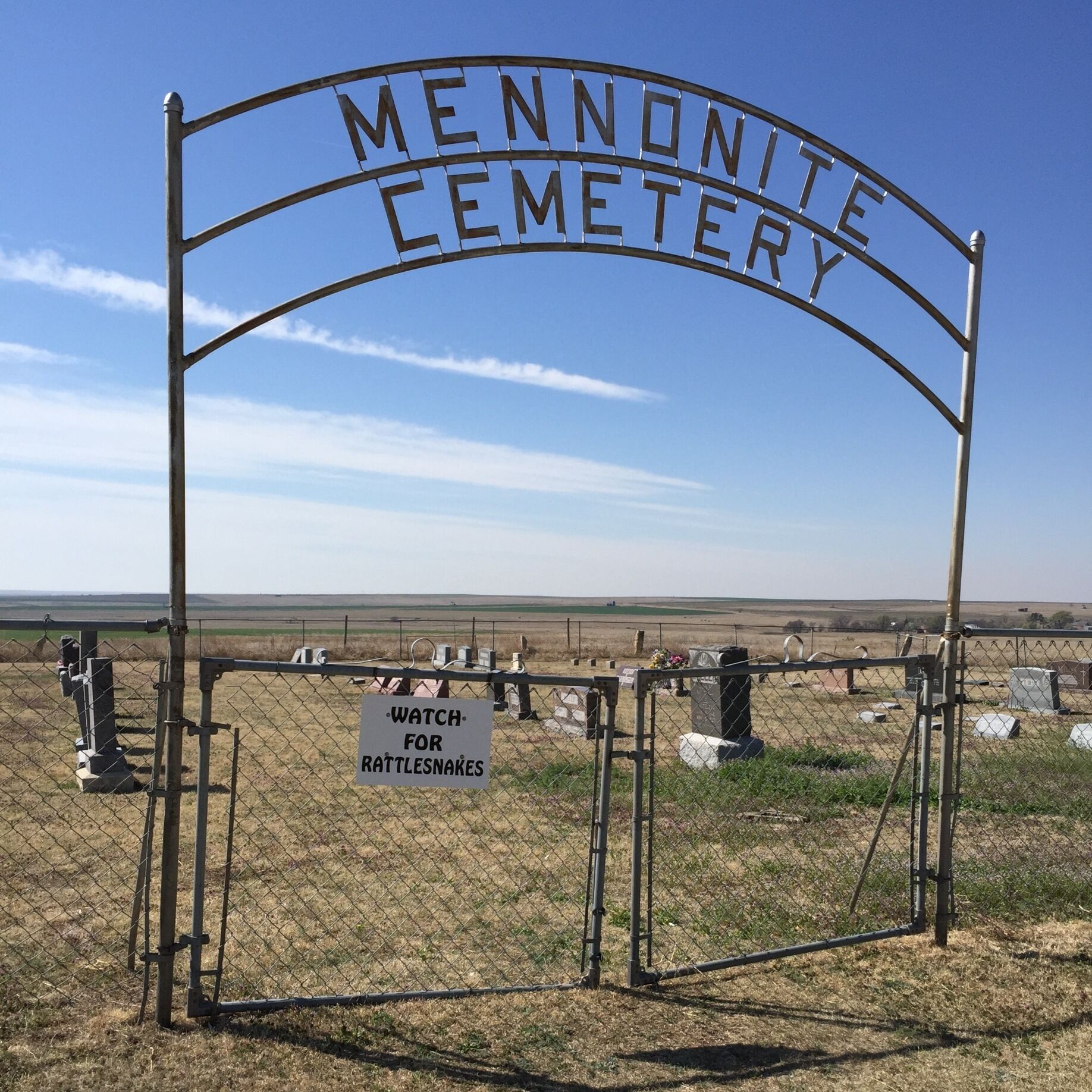 A cemetery gate with a sign warning to watch for rattlesnakes.