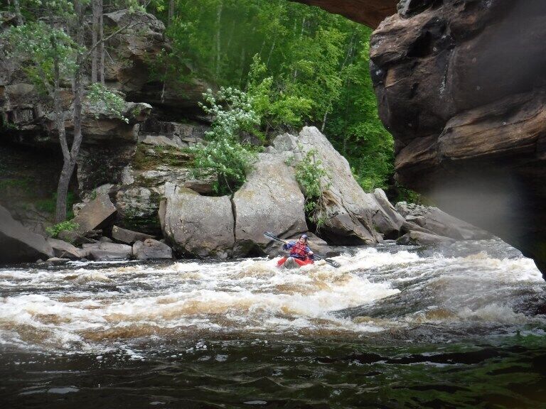 A kayaker navigating a turbulent river surrounded by rocky terrain and dense greenery.