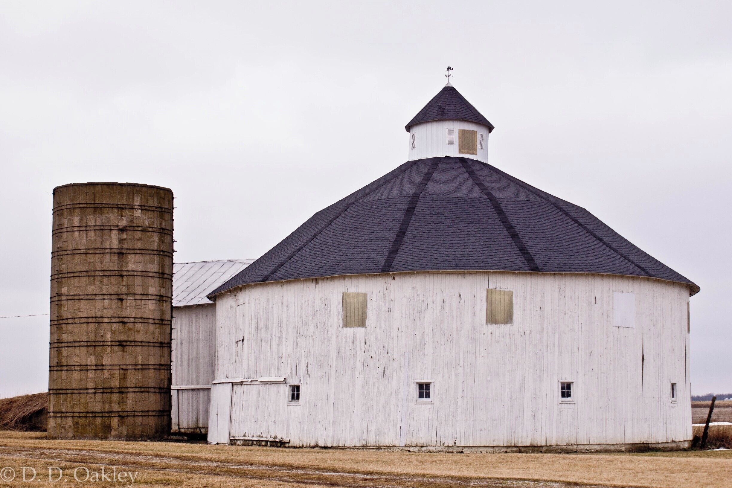 A white barn with a conical roof and a cylindrical silo.