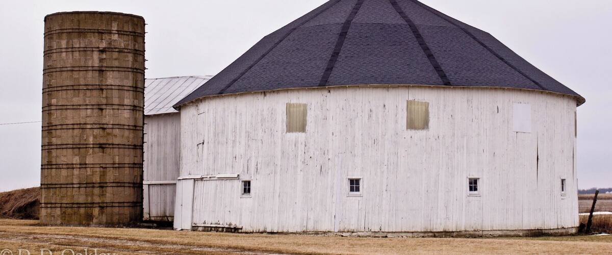 A white barn with a conical roof and a cylindrical silo.