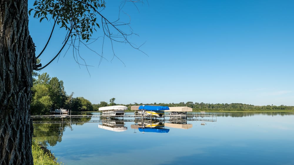 Docked boats on lifts are reflected in the calm water of a pretty lake in Minnesota, on a sunny summer day with beautiful clear blue sky.