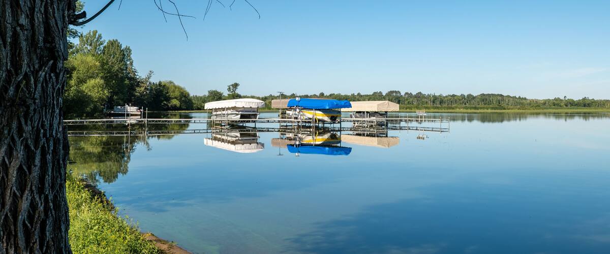 Docked boats on lifts are reflected in the calm water of a pretty lake in Minnesota, on a sunny summer day with beautiful clear blue sky.