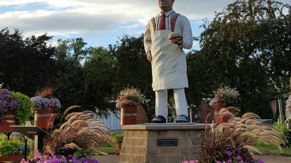 A statue of a man in traditional attire on a pedestal, surrounded by potted plants and flowers.