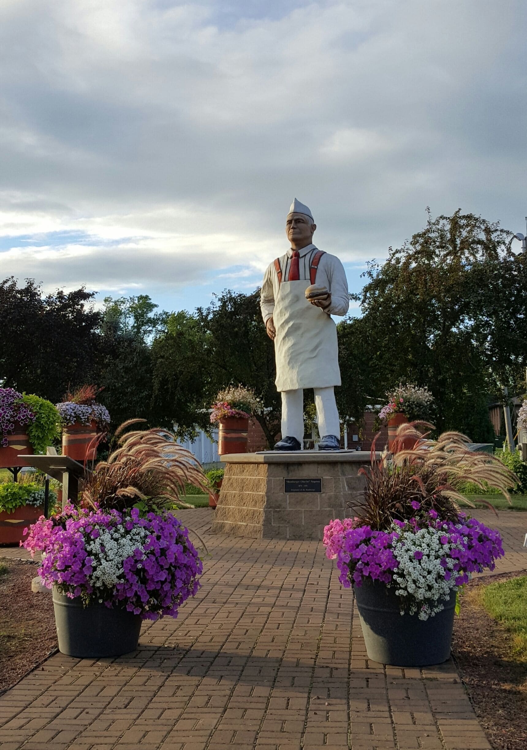 A statue of a man in traditional attire on a pedestal, surrounded by potted plants and flowers.