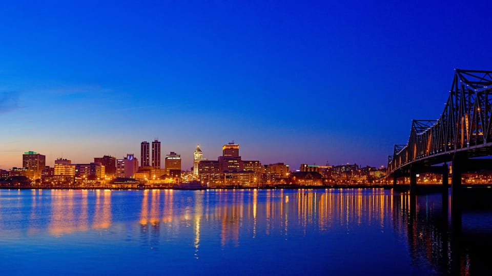 A city skyline at dusk with a bridge reflecting on the water.