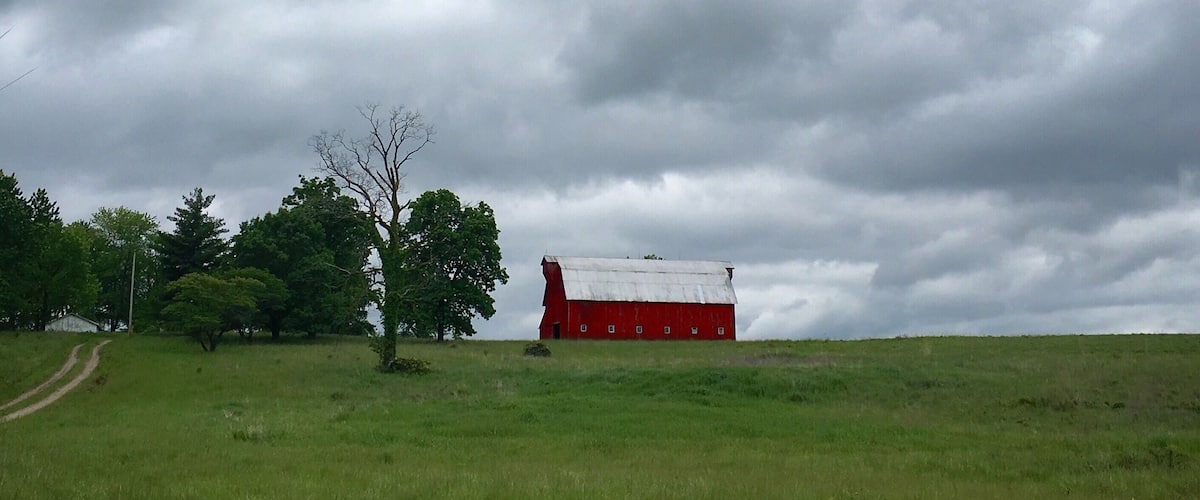 A red barn in a grassy field with a cloudy sky.