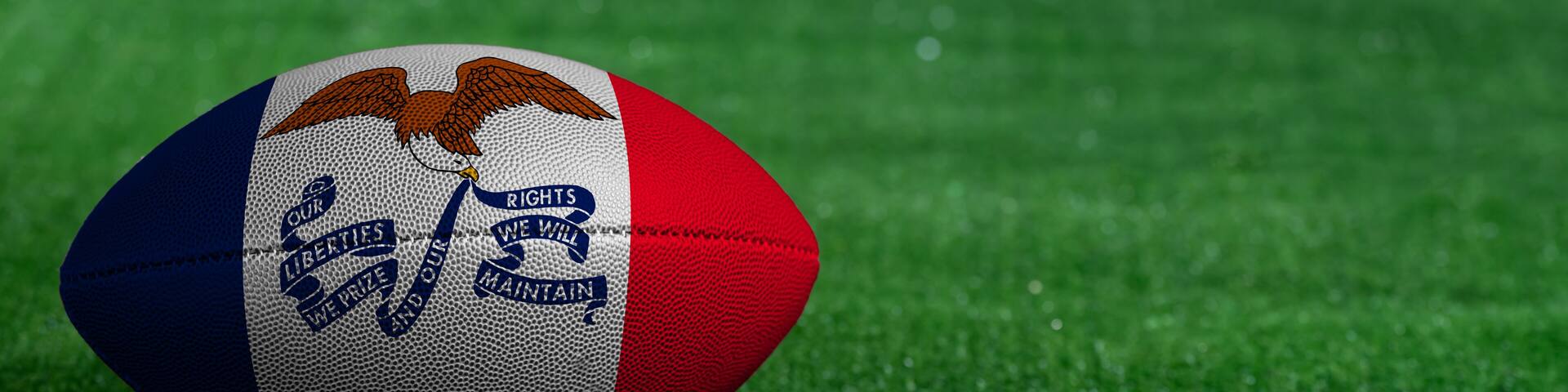 American football ball with Iowa flag on green grass background, close up