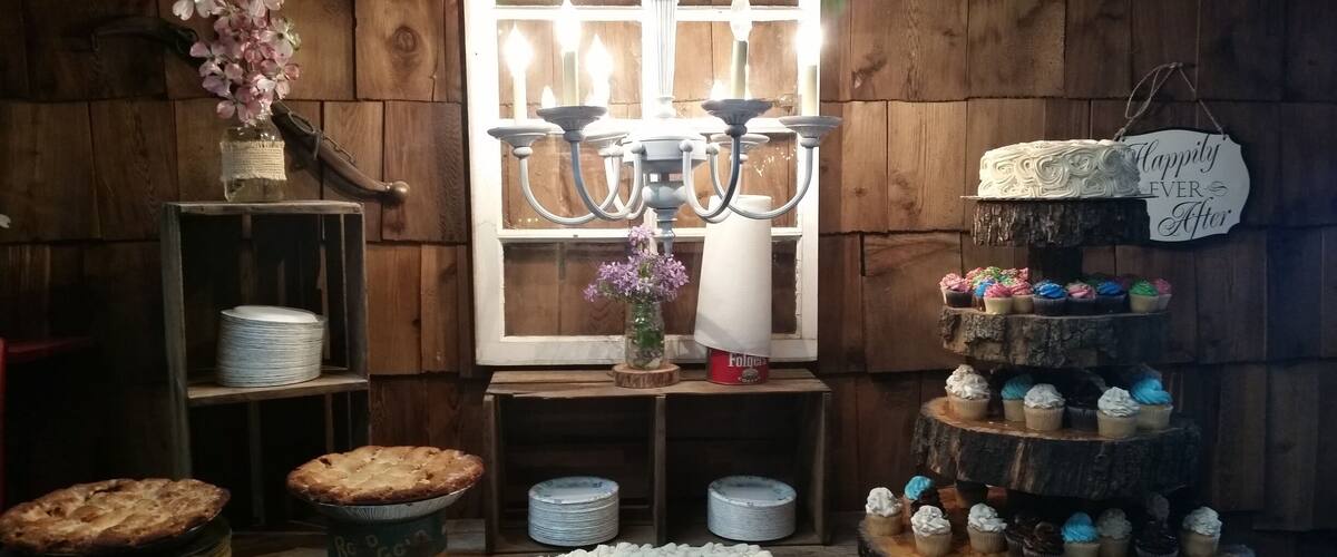 A rustic kitchen with wooden walls, a chandelier, a cake stand with cupcakes, and a pie on a wooden table.