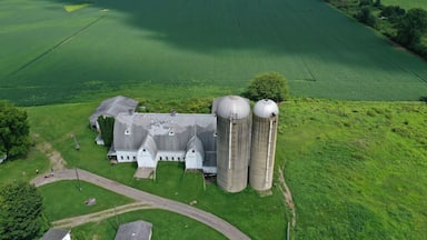 An aerial view of a farm with large silos, a barn, and expansive green fields.