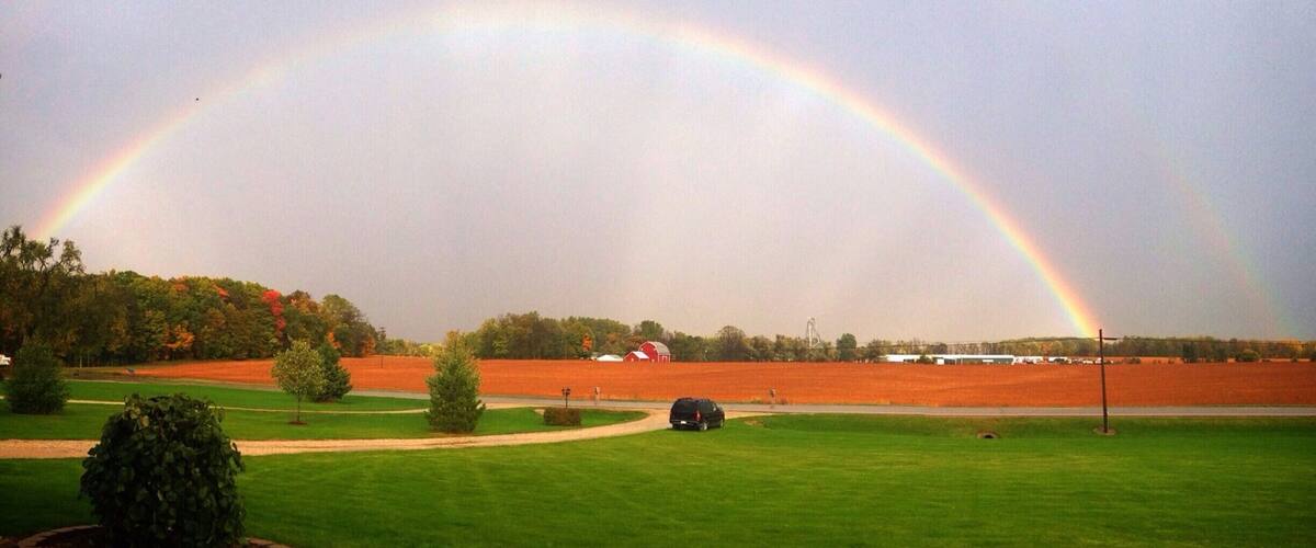 A rainbow over a field with a car and a red barn.