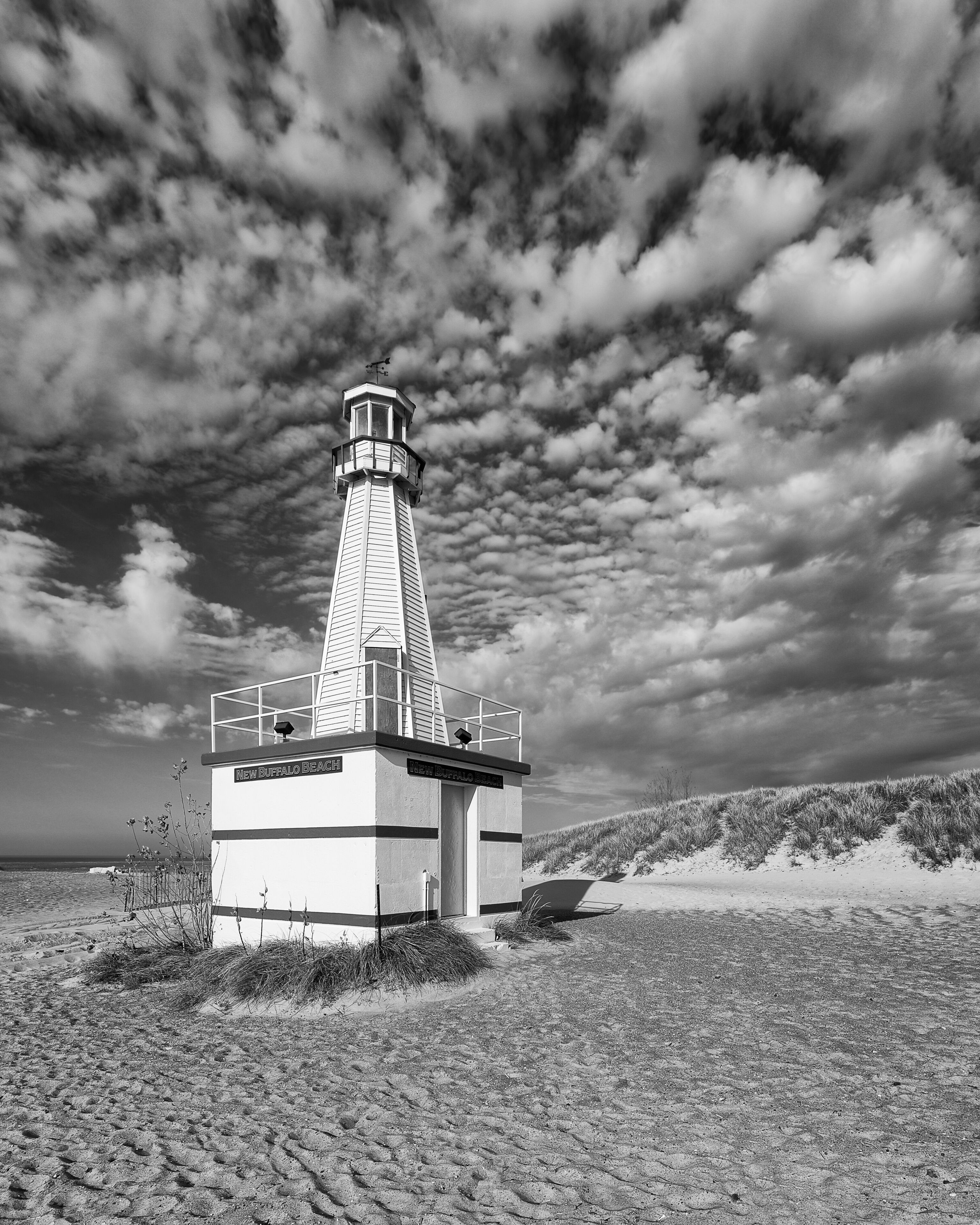 A lighthouse on a sandy beach with a cloudy sky.