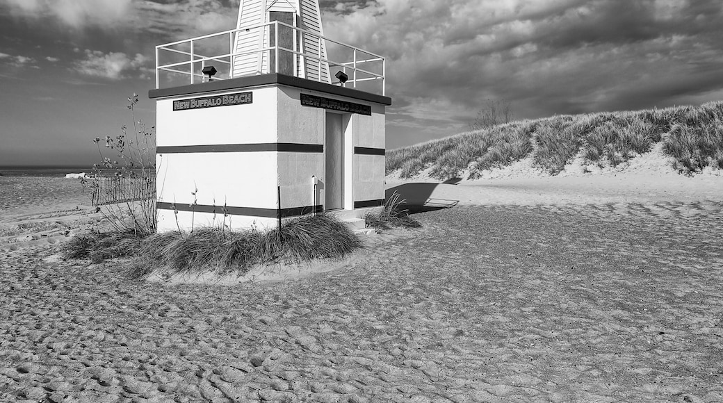 A lighthouse on a sandy beach with a cloudy sky.