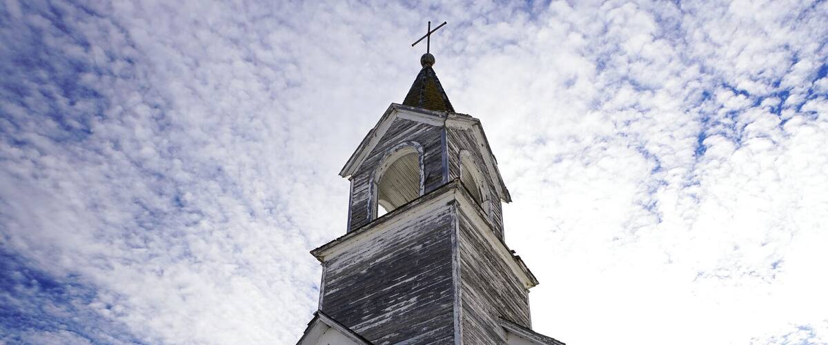 A weathered wooden church with a steeple and a cross, surrounded by snow.