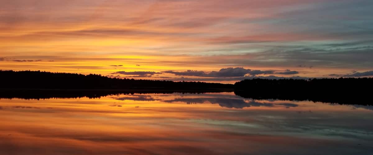 A sunset over a calm lake with a forested shoreline.