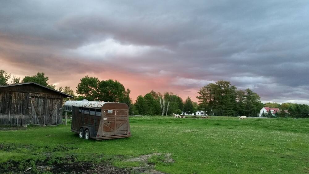 Un paysage rural avec une caravane, une grange et des chevaux qui paissent sous un ciel nuageux.