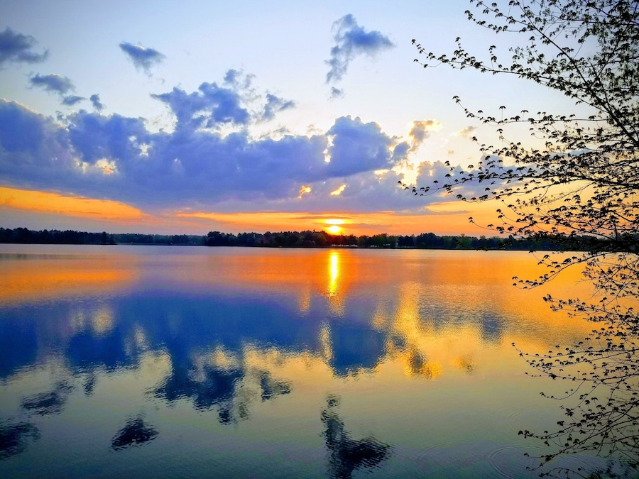A calm lake at sunset with a reflection of the sky and trees on the water's surface.