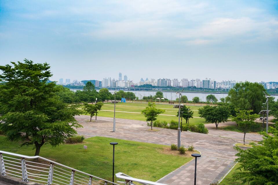 Um parque com caminhos, árvores e a silhueta distante de uma cidade.