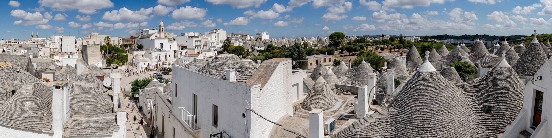 A coastal town with white buildings and distinctive conical roofs, under a clear blue sky.