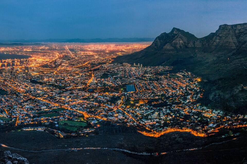 A mountainous landscape with a city at its base, a coastline, and a sunset.