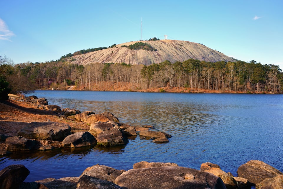 Um lago com uma colina imponente ao fundo, rodeado por árvores e pedras.