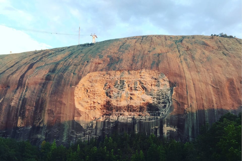 A large rock formation with a carved face, surrounded by a park with people and trees.