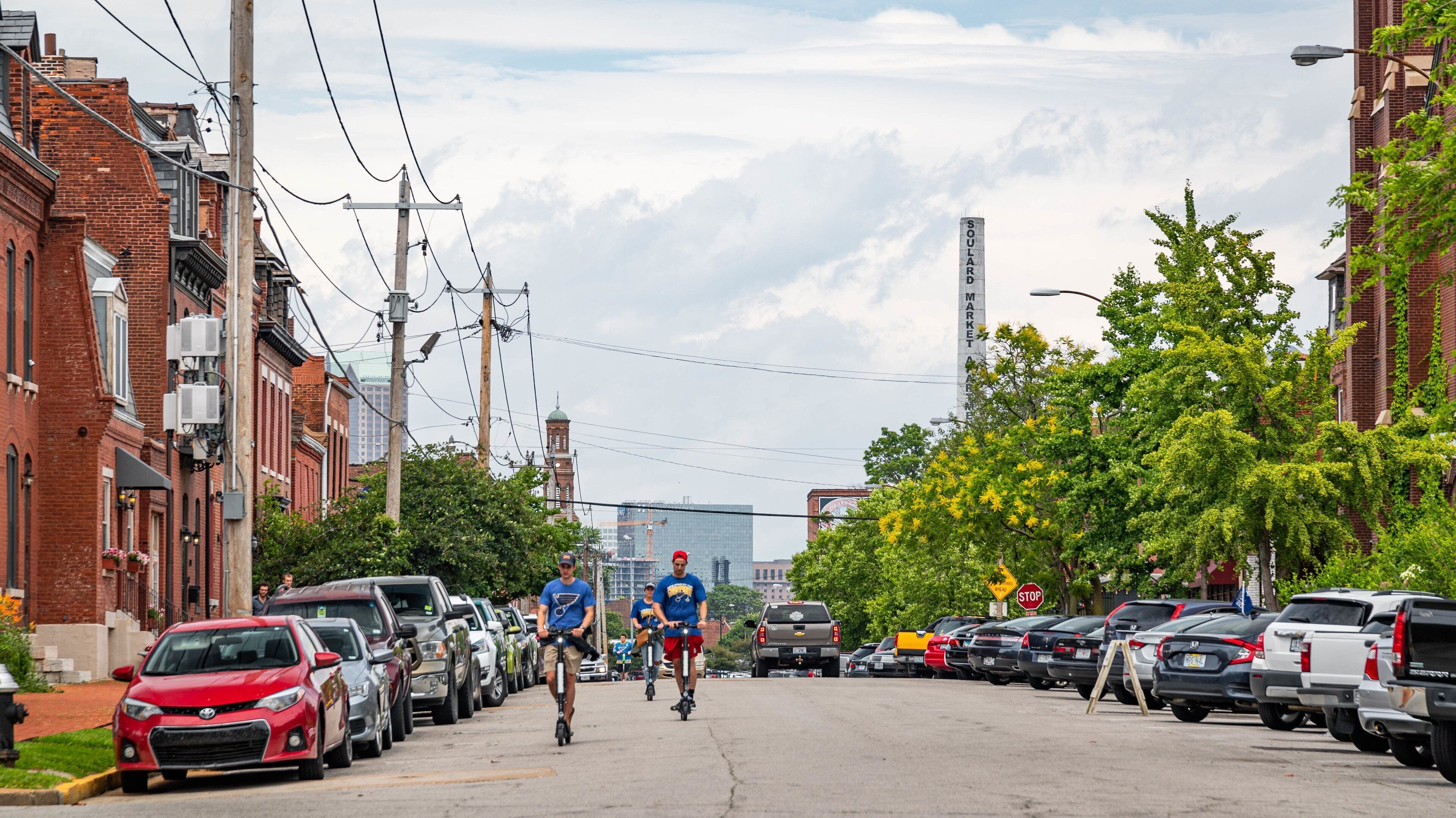 A street lined with parked cars and buildings, a cyclist in the foreground, and a large sign reading "SOULARD MARKET" in the background.