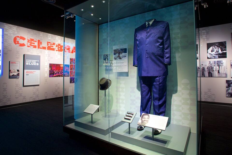 Een museumexpositie met een blauw pak in etalage, omringd door informatieposters en een glazen vitrine.