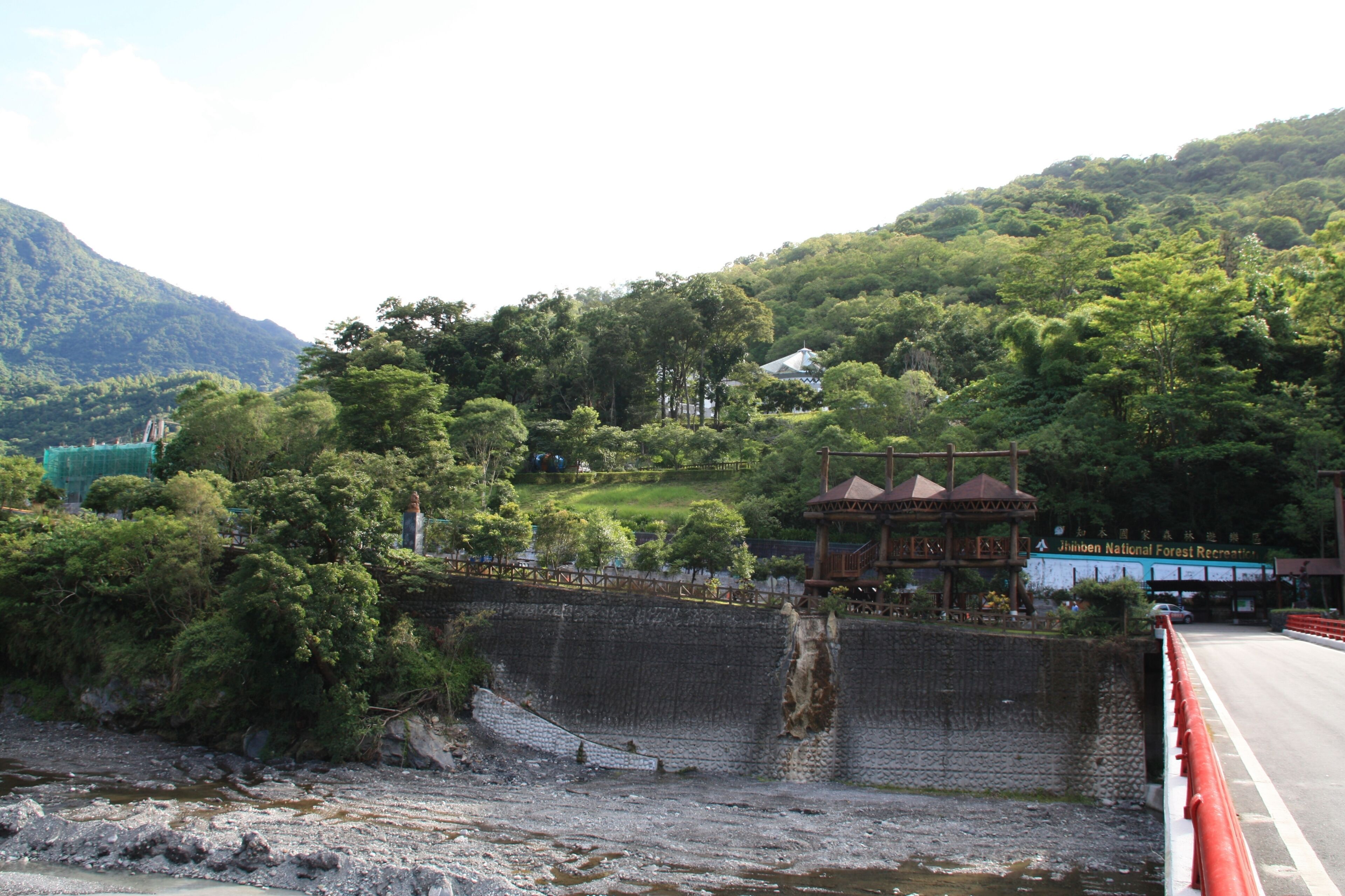 A scenic view of a river with a bridge, lush greenery, and a mountain in the background.