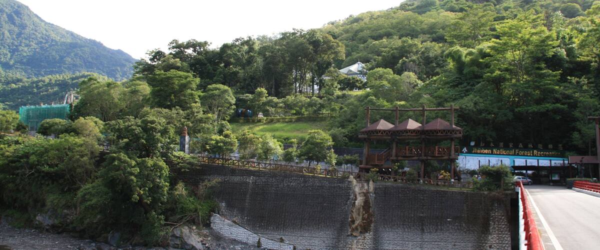 A scenic view of a river with a bridge, lush greenery, and a mountain in the background.