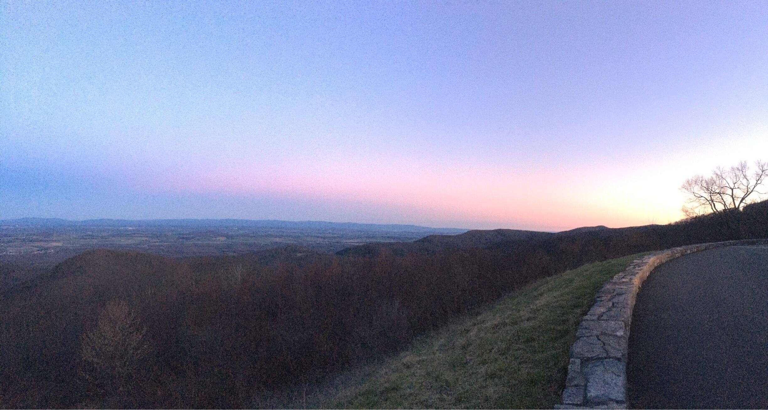 A sunset view over a hilly landscape with a stone wall and a road.