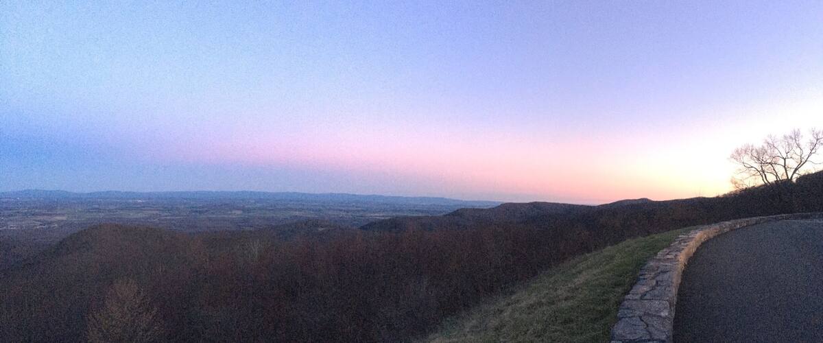 A sunset view over a hilly landscape with a stone wall and a road.