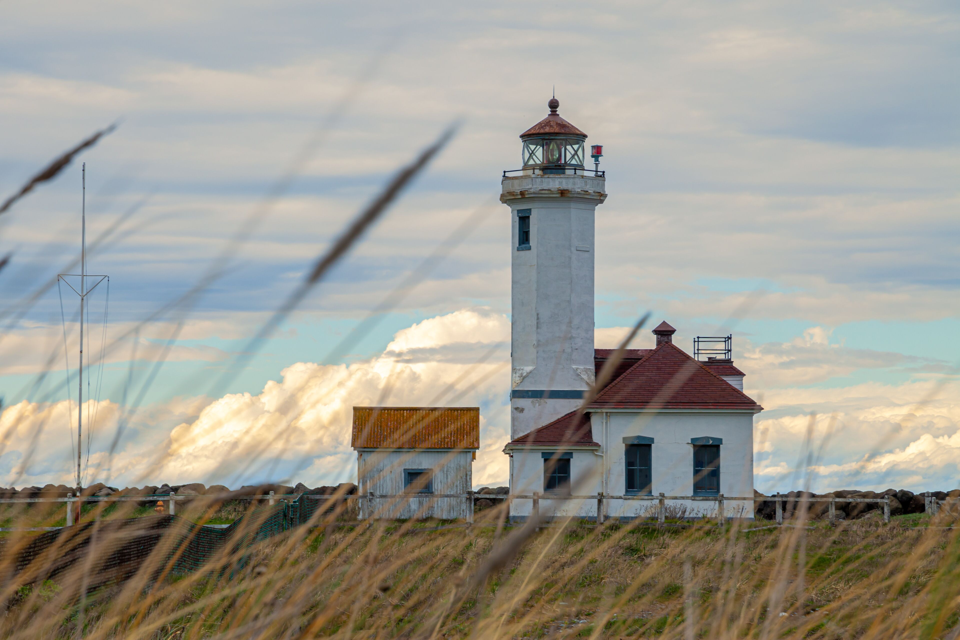 A lighthouse with a red roof and a white tower, surrounded by grass and rocks.