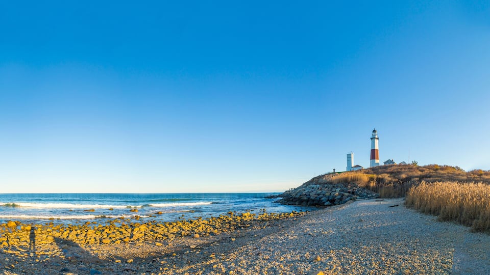 A rocky beach with a lighthouse on a hill.