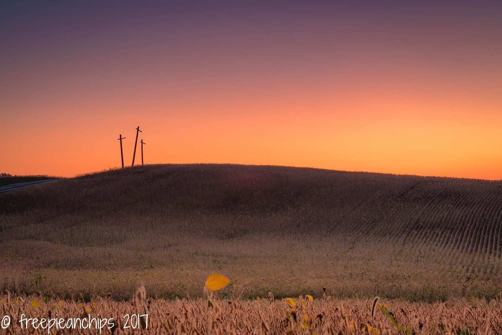 A sunset over a hilly landscape with three crosses on a hill.