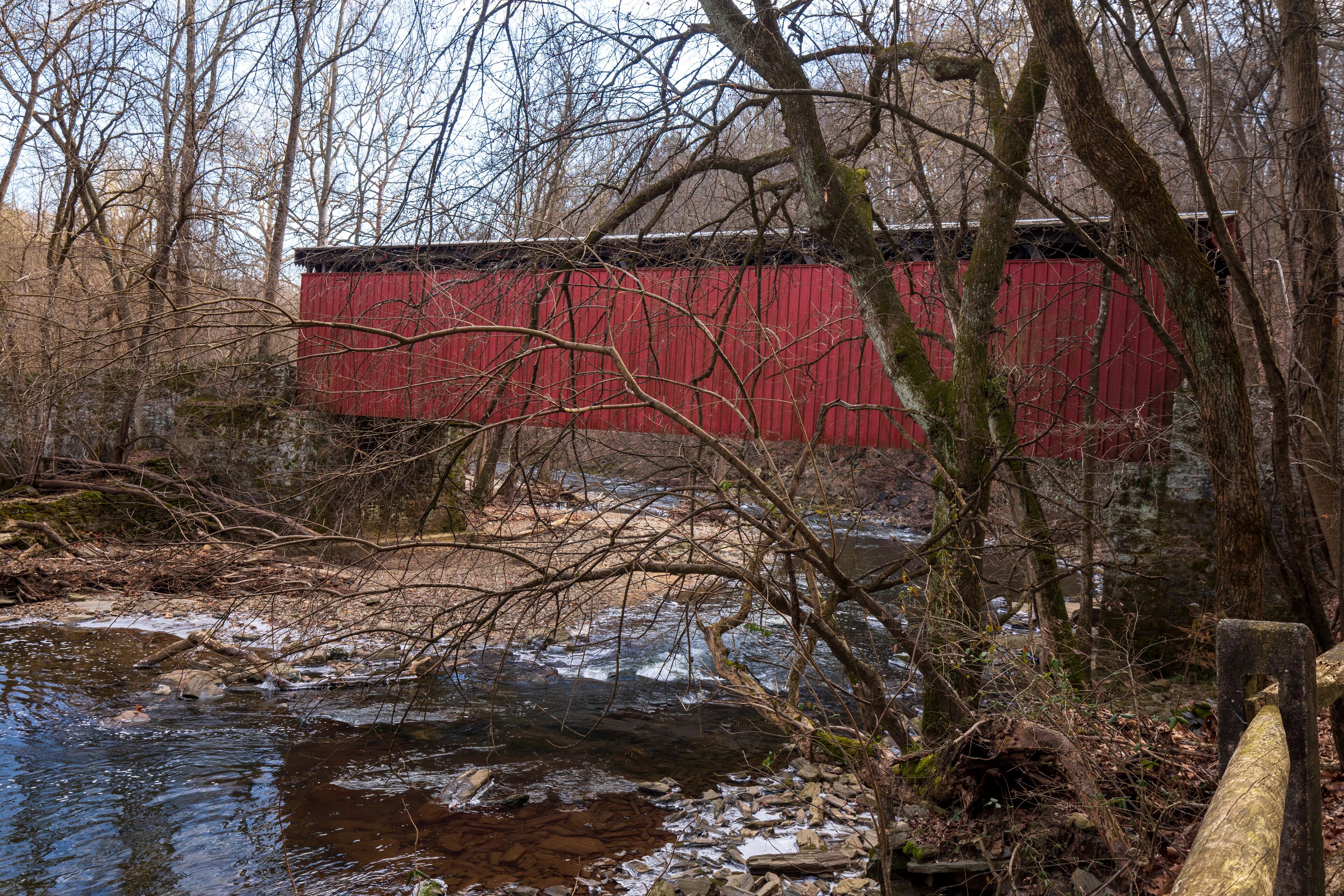 A red wooden structure near a flowing stream in a wooded area.