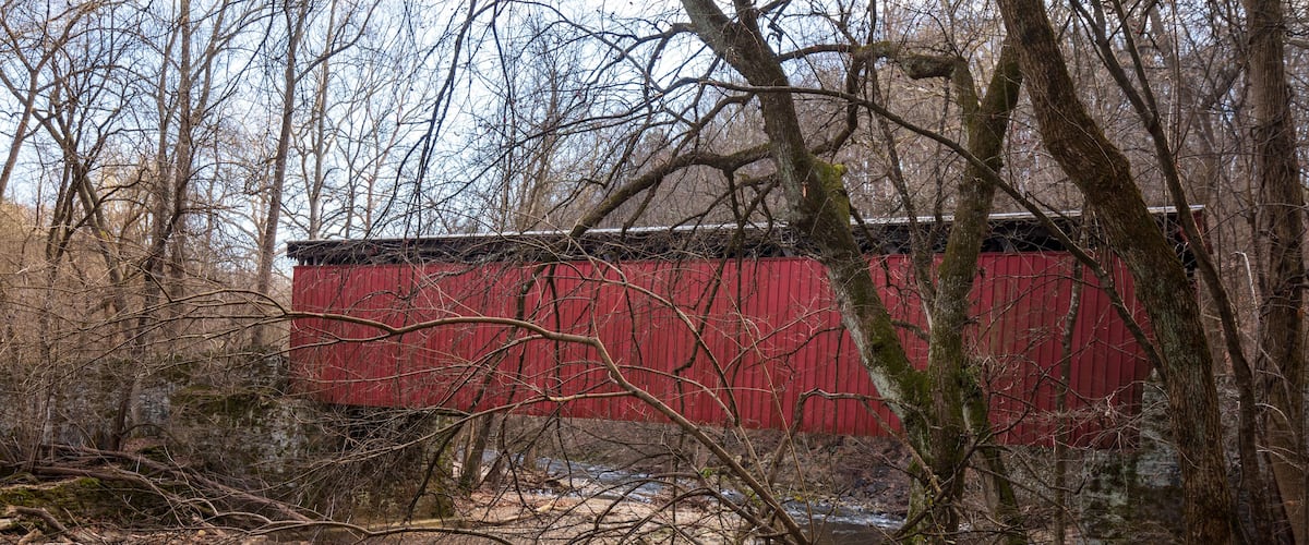 A red wooden structure near a flowing stream in a wooded area.